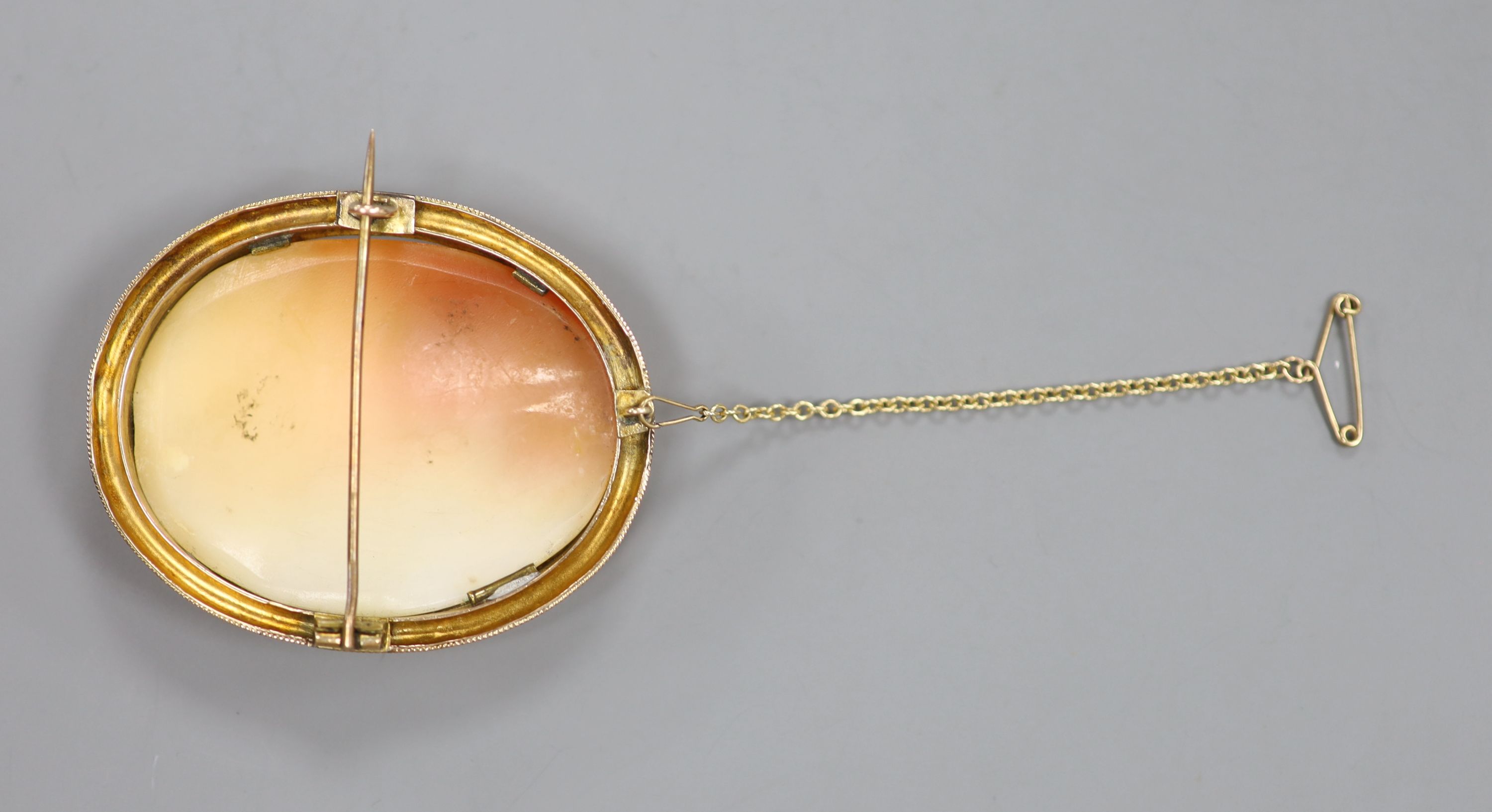 A yellow metal mounted oval cameo shell brooch, carved with scene of two ladies in a garden, 55mm, gross 19.3 grams.